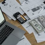A desk with financial documents, currency, a laptop, and phone calculator. passive income streams