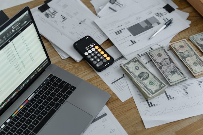 A desk with financial documents, currency, a laptop, and phone calculator. passive income streams