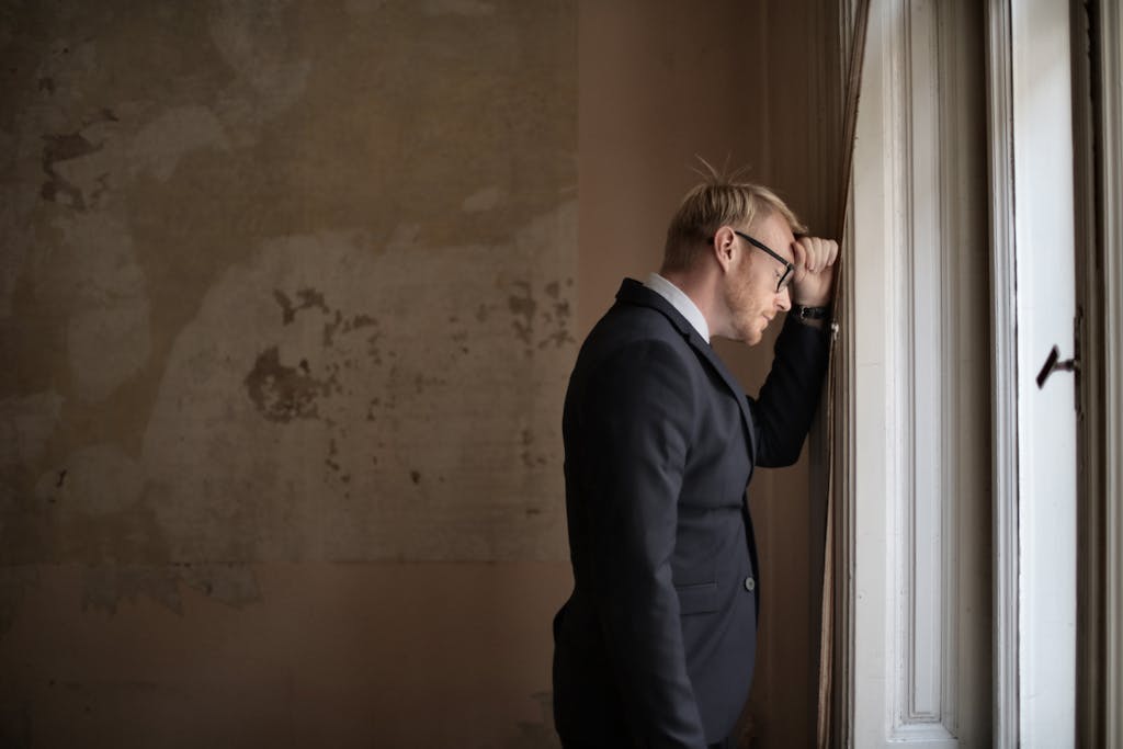 A worried businessman in a suit leaning against a window, expressing stress and concern. financial mistakes