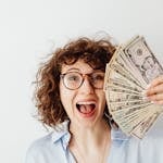 Caucasian woman with curly hair delights in holding US dollars against a white background. Money Hacks
