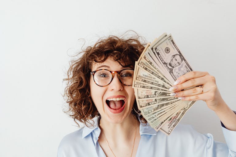 Caucasian woman with curly hair delights in holding US dollars against a white background. Money Hacks