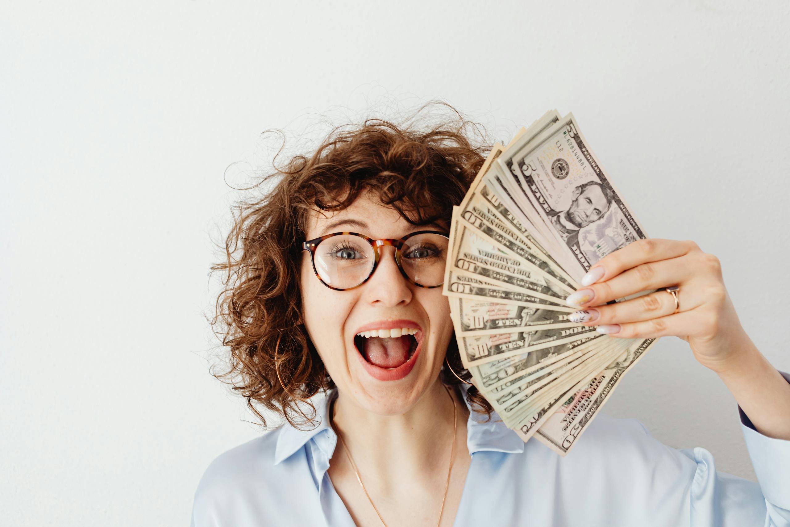 Caucasian woman with curly hair delights in holding US dollars against a white background. Money Hacks