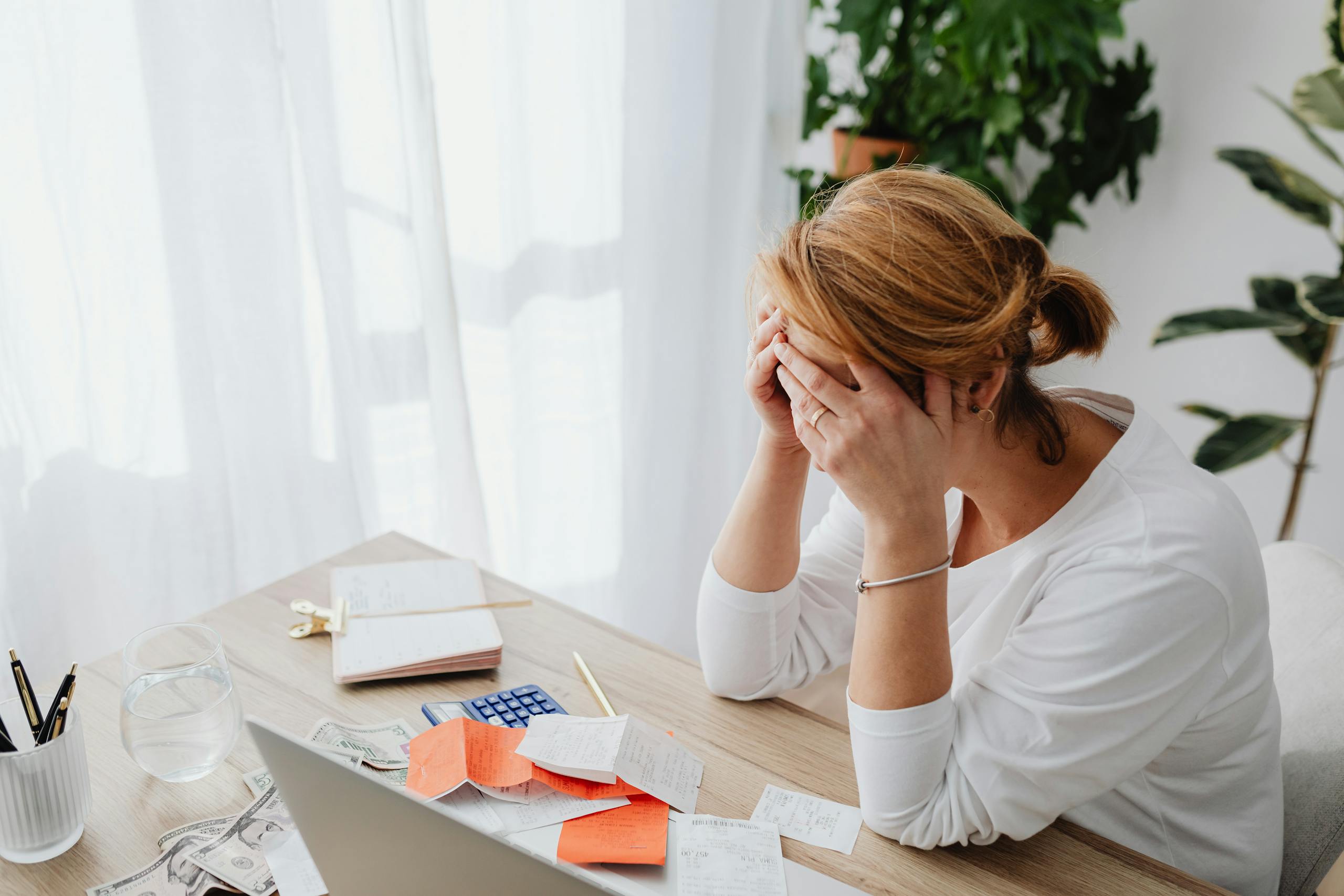 Woman stressed over financial mistakes at a desk, dealing with expenses and calculations.